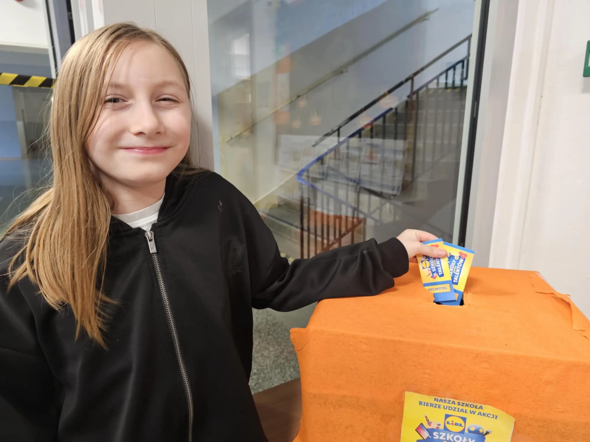 Uczennica wrzuca talenciaki do pudełka wykonanego przez uczniów